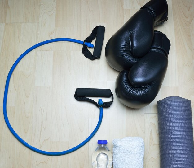 Rope in shape g kick boxing gloves bottle of water towel and rollable mattress on wooden background