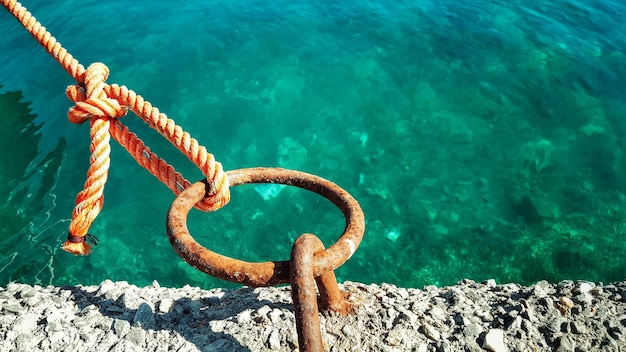 Photo rope tied on rusty mooring ring at harbor