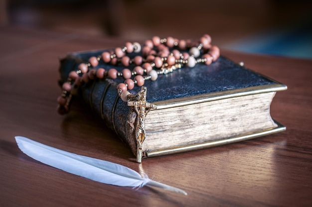 Rosary on the old Bible and white feather