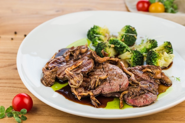 Rosbief met champignons en broccoli in een plaat op een lichte houten ondergrond.