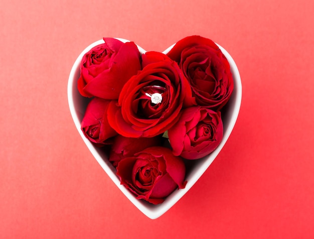 Кольцо с розой и бриллиантом внутри чаши в форме сердца на красном фоне
