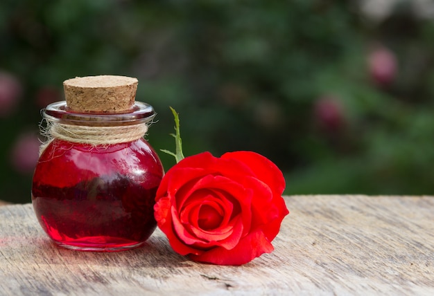 Rose essential oil in a round bottle and red rose