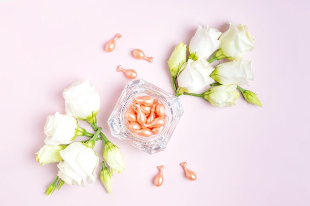 분홍색 배경에 유스토마 꽃 성분이 있는 유리병에 얼굴용 화장품 오일이 포함된 로즈 골드 캡슐은 패키지 여행 화장품 개념을 사용합니다.