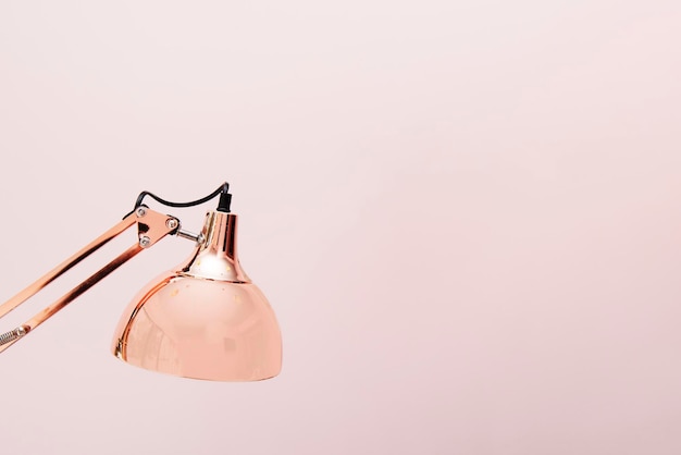 A rose gold folding lamp with a plain pink background