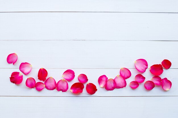 Rose petals on white wooden background.