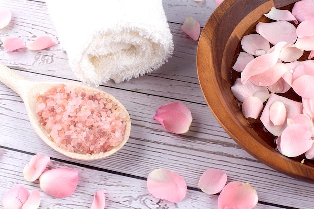 Rose petals on a wooden bowl with pink salt andwhite towel on wooden background