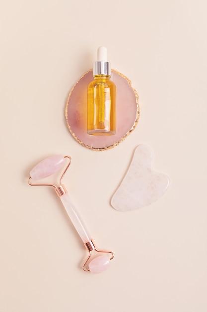 Rose quartz face roller, gua sha stone, essential oil. Natural skin care concept. Top view, flat lay