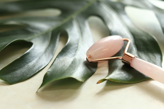 Rose quartz facial massage roller closeup Massage roller on a monstera leaf and candles side view