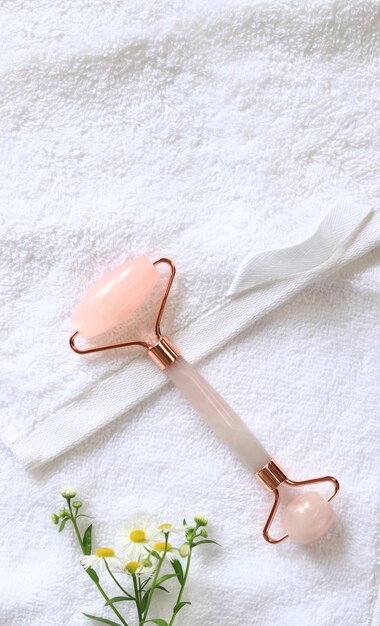 Rose quartz gezichtsroller Roller voor cosmetische gezichtsmassage kamomille en witte handdoek Flat lay