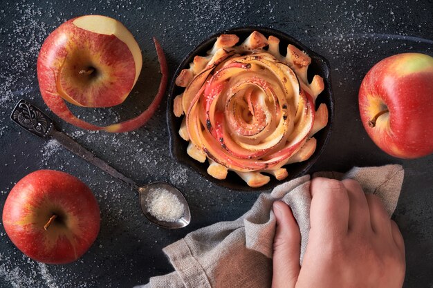 Rose shaped appelgebak in ijzer koekepan op donker met sommige appels en suiker