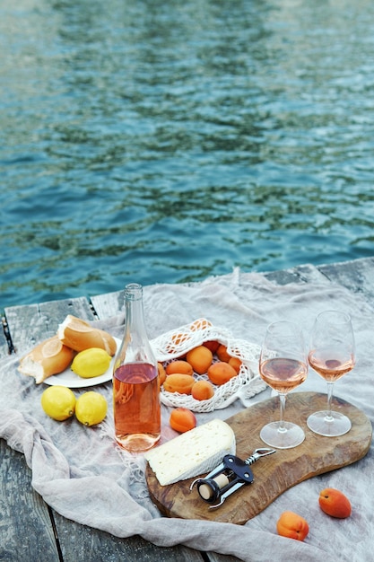 Foto frutta e snack al vino rosato sul molo di legno durante il pittoresco picnic sul molo di legno