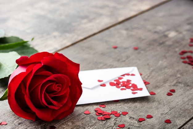 Rose with envelope and hearts on wooden background