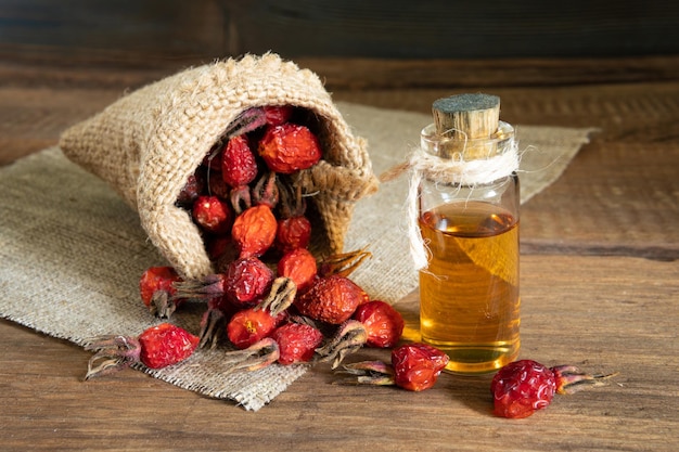 Rosehip oil on wooden background with red fruits