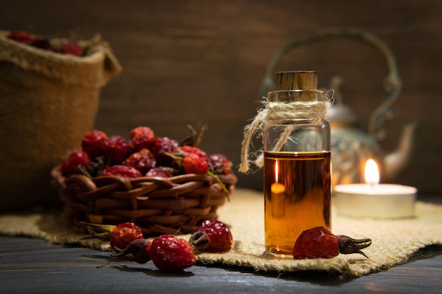 Rosehip oil on wooden boards on a dark background. The bottle is tied with a cord with dogrose essential oil. The candle is on.