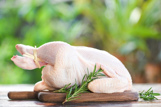ローズマリー鶏肉-自然の緑の背景に木製のまな板で全体の新鮮な生の鶏肉