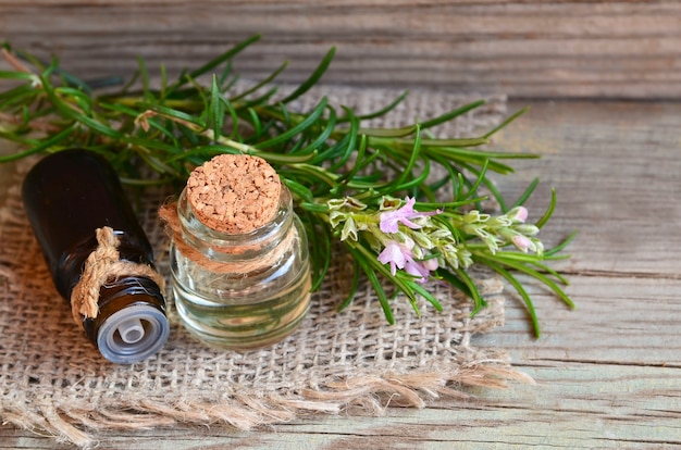 Rosemary etherische olie in glazen flessen met vers groen rozemarijnkruid op oud hout