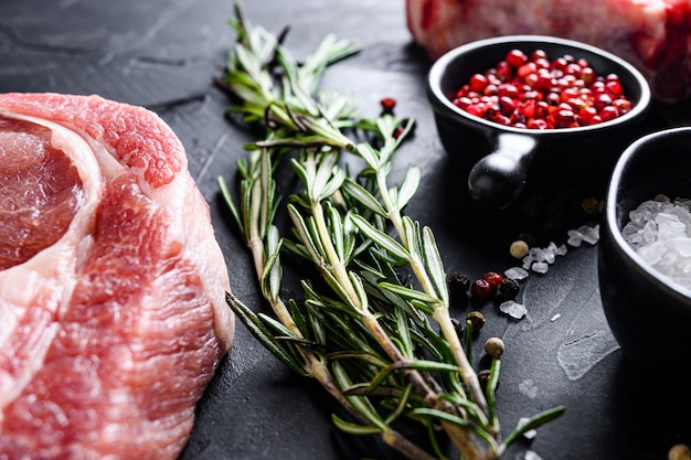 Rosemary herbs close up on black stone table with spices and raw meat near side view selective focus