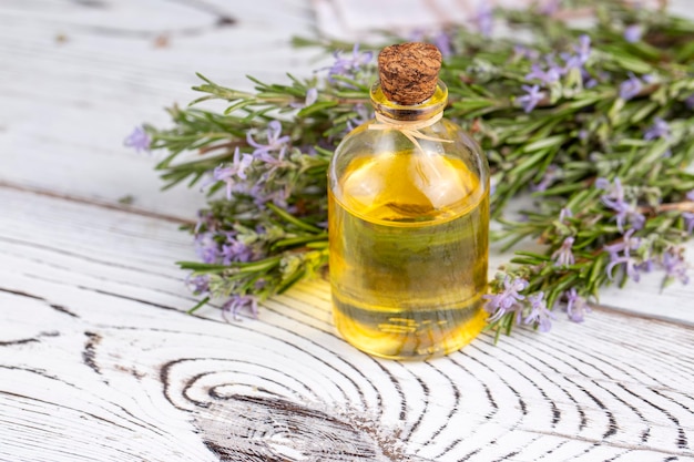 Rosemary oil Rosemary essential oil jar glass bottle and branches of plant rosemary with flowers on rustic background