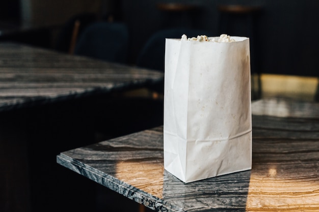 Rosemary Popcorn in paper bag on top marble table on the left side 