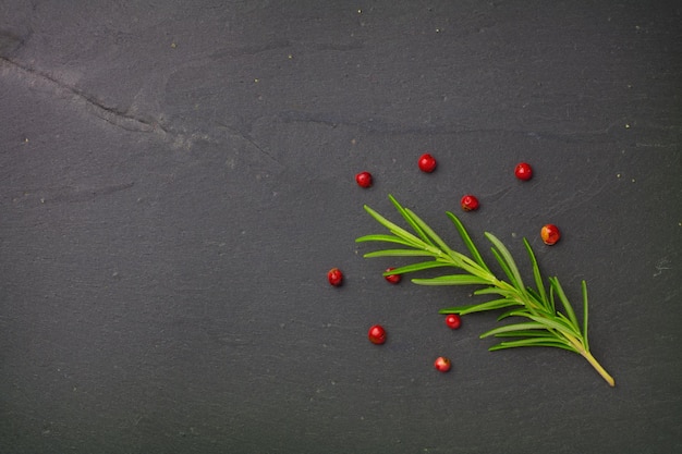 Rosemary and red pepper seeds on gray stone plate.