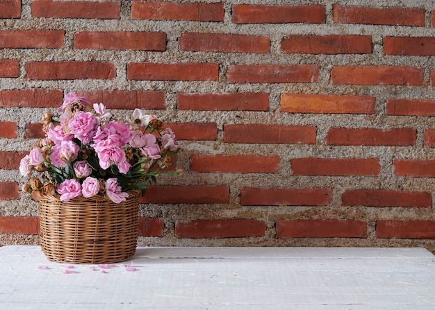 Merce nel cestino delle rose sulla tavola di legno contro il muro di mattoni