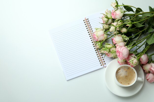 Roses, cup of coffee and copybook on white