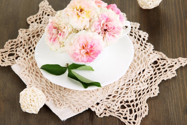 Roses in cup on napkins on wooden background