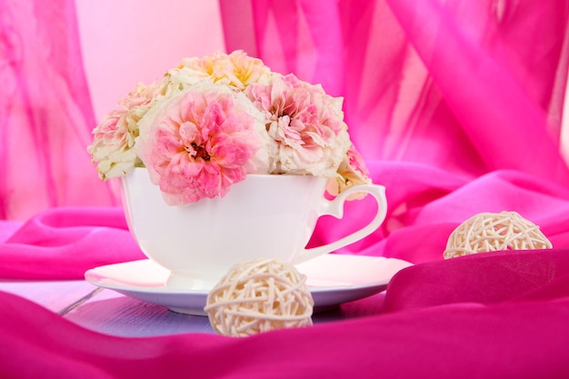 Roses in cup on wooden table on pink cloth background