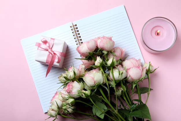 Roses, gift box, copybook and candle on pink