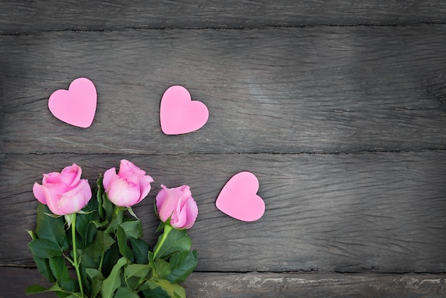 Roses with hearts on a wooden background. Pink flowers with pink hearts with copy space on dark wooden background