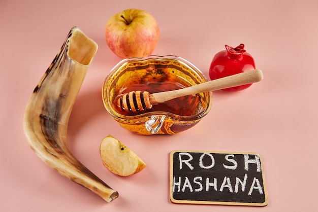 Photo rosh hashanah lettering jewish new year holiday concept bowl in the shape of an apple with honey apples pomegranates shofar on pink background