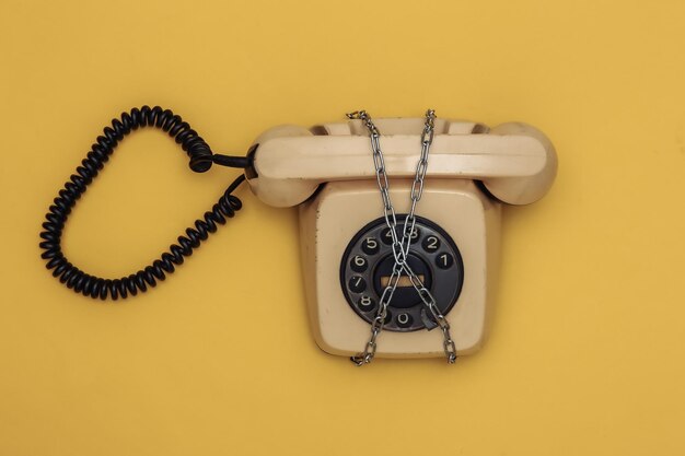Rotary telephone wrapped in a steel chain on yellow background. Top view