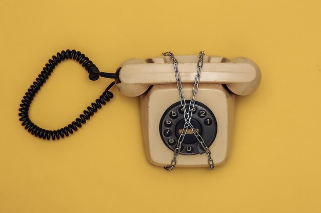 Telefono rotante avvolto in una catena di acciaio su sfondo giallo. vista dall'alto