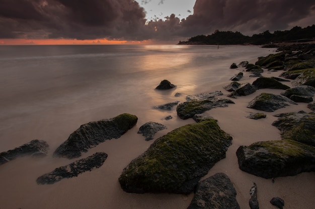 Rots op donker strand met damatische wolk in ochtend met zonsopgang