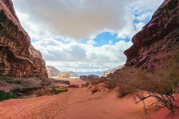 Rotsachtige kloof met rood zand op de grond, blauwe lucht in de verte - Wadi Rum-landschap