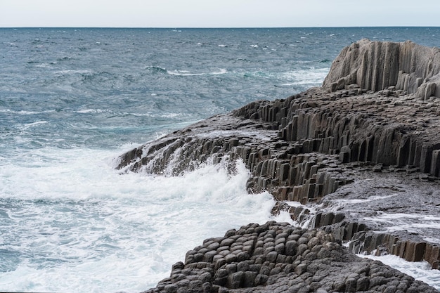 Rotsachtige kust gevormd door zuilvormig basalt tegen de achtergrond van een stormachtig zeekustlandschap van de Koerilen-eilanden