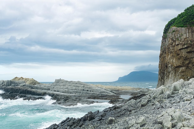 Rotsachtige kust gevormd door zuilvormig basalt tegen de achtergrond van een stormachtig zeekustlandschap van de Koerilen-eilanden