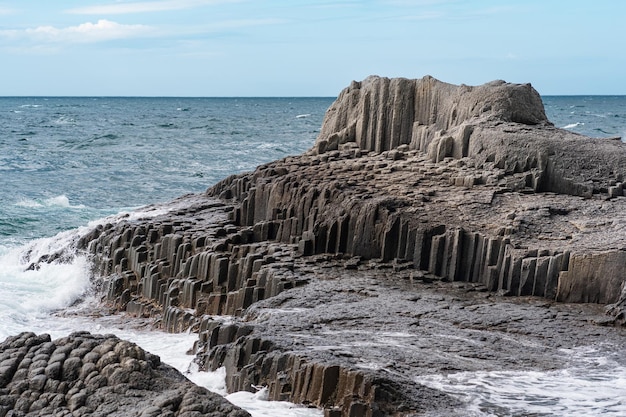 Rotsachtige kust gevormd door zuilvormig basalt tegen het stormachtige zeekustlandschap van de Koerilen-eilanden