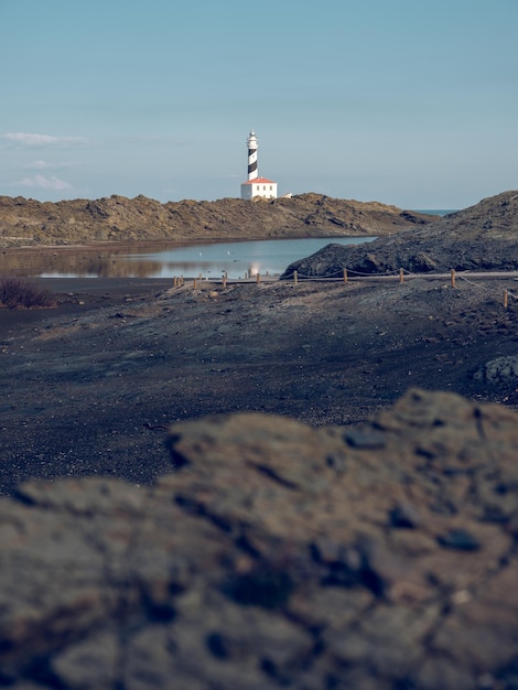 Rotsachtige oever van een vredig meer met verre vuurtoren tegen de blauwe lucht op het platteland