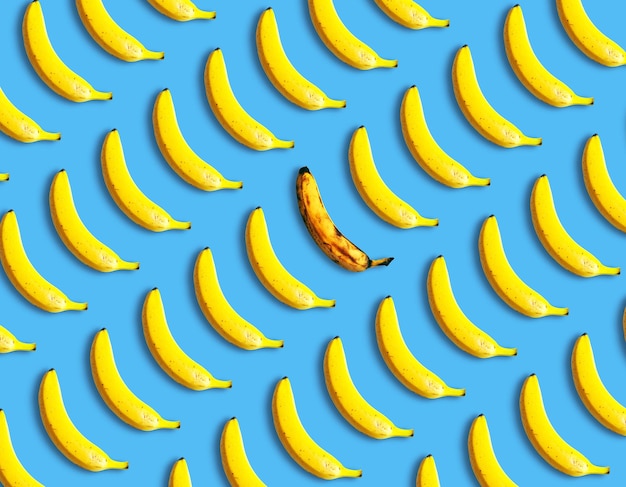 Rotte banaan ligt tussen verse bananen op een blauwe achtergrond bovenaanzicht Uniek creatief idee Niet zoals iedereen concept