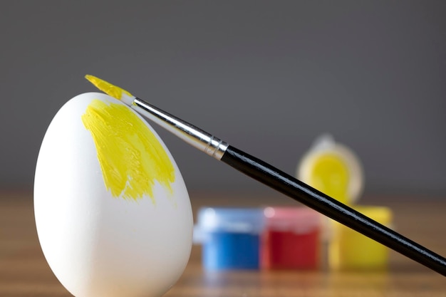 Photo rough brush is painting a fragile easter egg with yellow color prepering for holiday happy easter