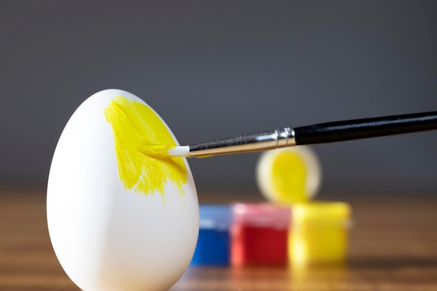 Photo rough brush is painting a fragile easter egg with yellow color prepering for holiday happy easter