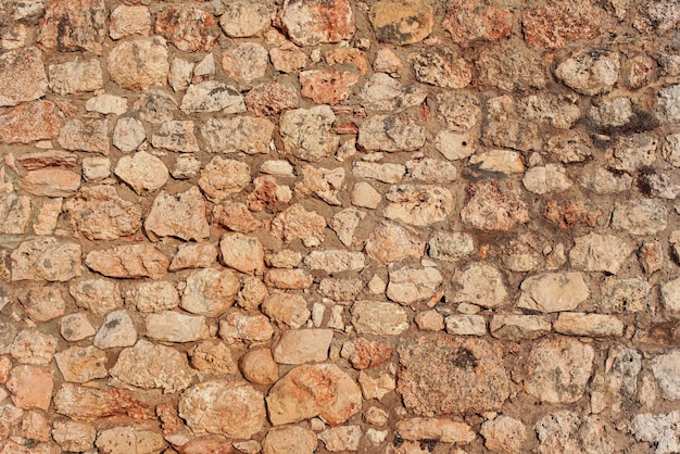 Rough reddish color stone bricks wall, sun shines on