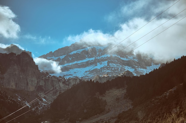 Rough rocky cliffs covered with white hoarfrost located in mountainous terrain with trees and power lines on cold winter day