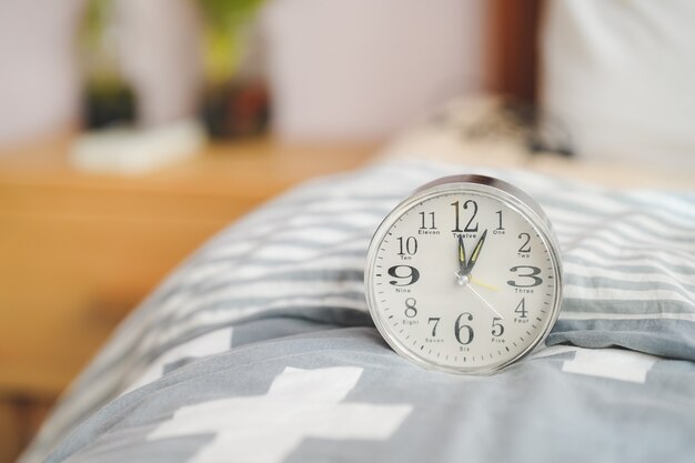 A round alarm clock sits on the blanket next to the bed. bedroom design.