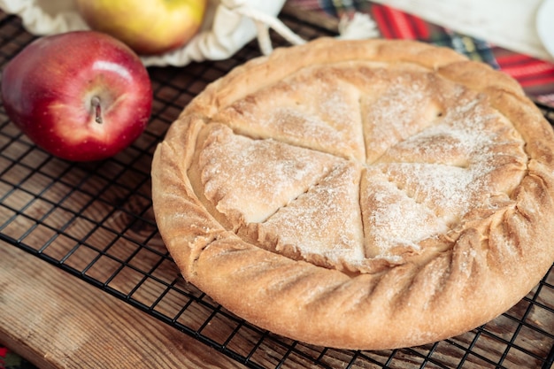 Torta di mele rotonda su fondo di legno con mele fresche in un sacchetto di tela