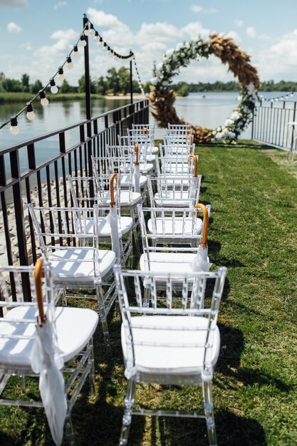 Round arch for a wedding ceremony by the river. White glass chairs stand for guests