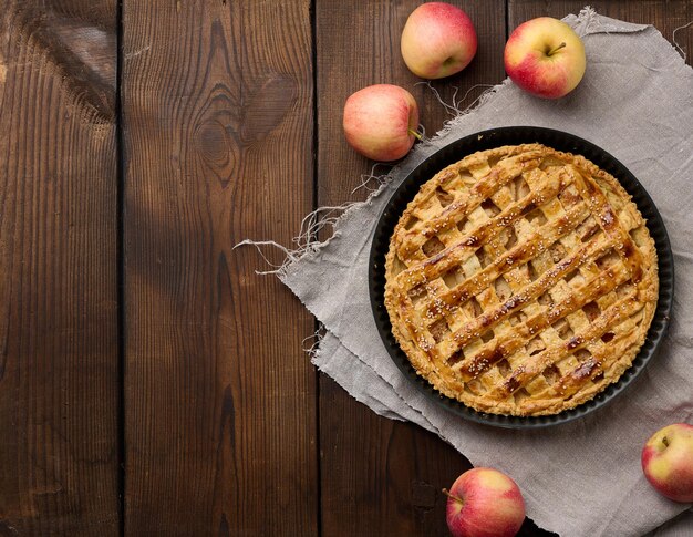 Round baked apple pie on a brown wooden table top view