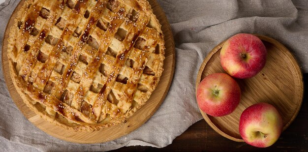 Round baked apple pie on a brown wooden table top view