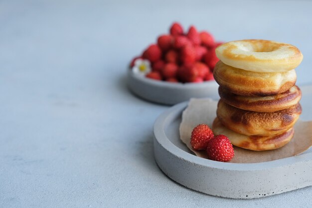 灰色のコンクリートの背景にイチゴと丸い焼きドーナツ。ミニマリズム。